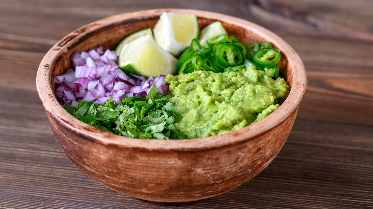 Chunky guacamole with avocado, lime and red onion, shown with optional cilantro and jalapeño garnishes